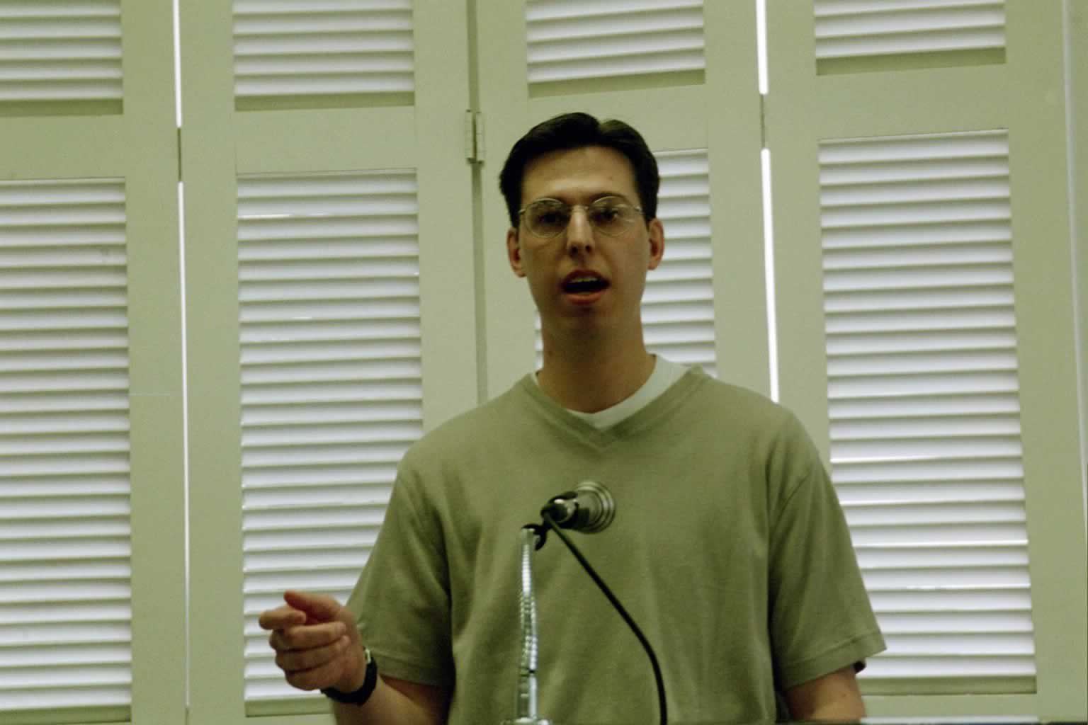 picture of man with glasses standing behind a podium talking