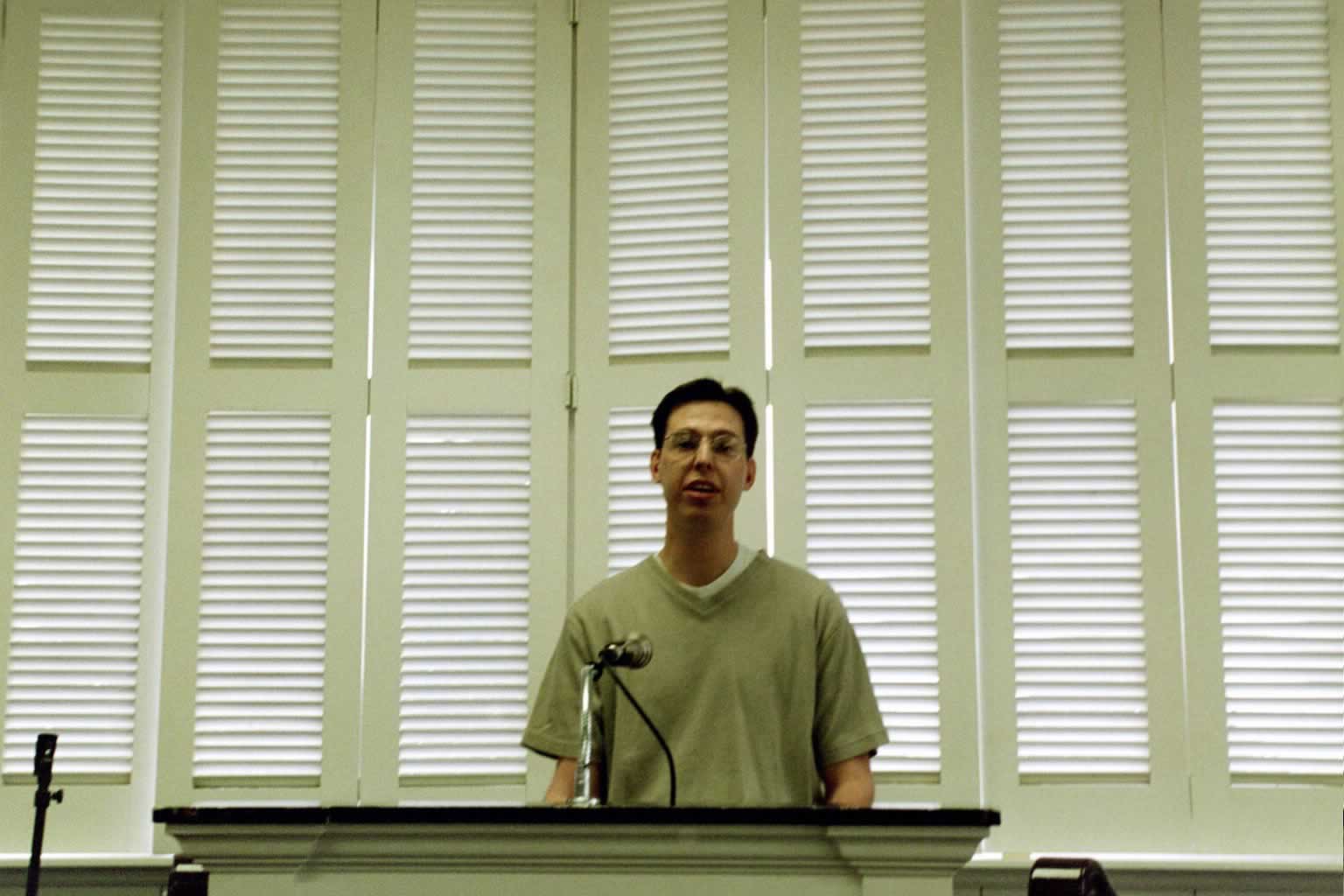 picture of man with glasses speaking behind a podium