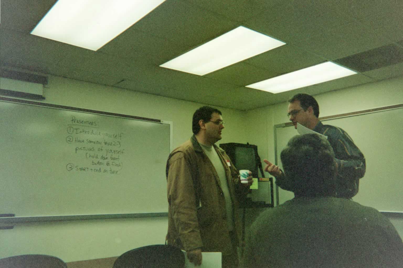 picture of three men gathered around speaking with each other