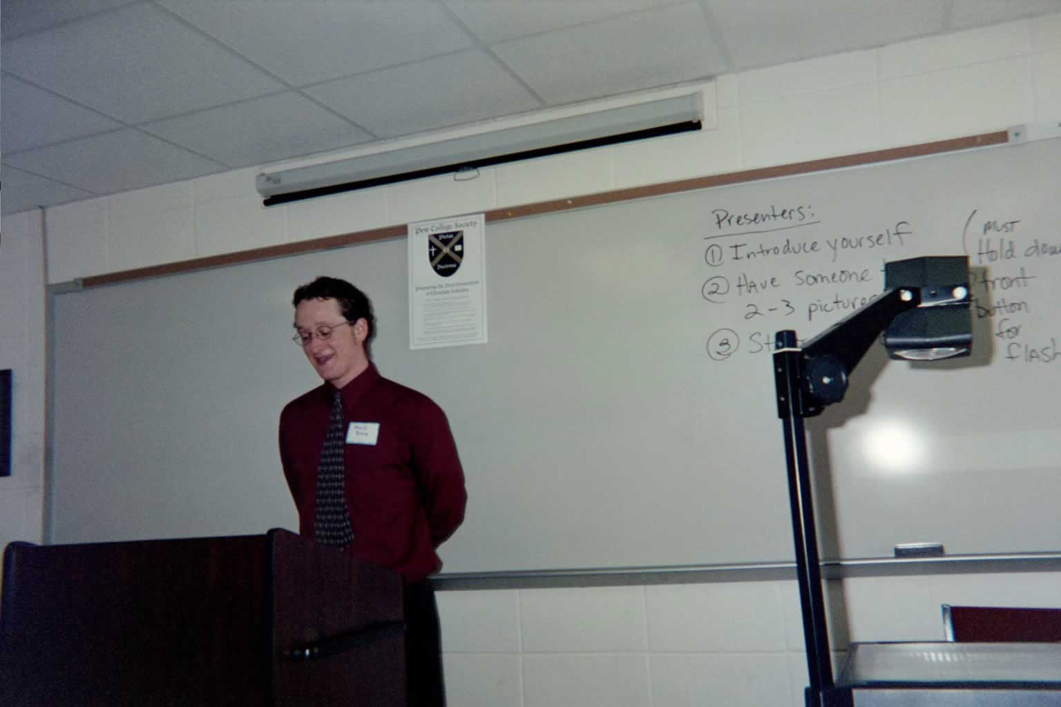 picture of a man wearing glasses and a red shirt standing behind a podium while speaking