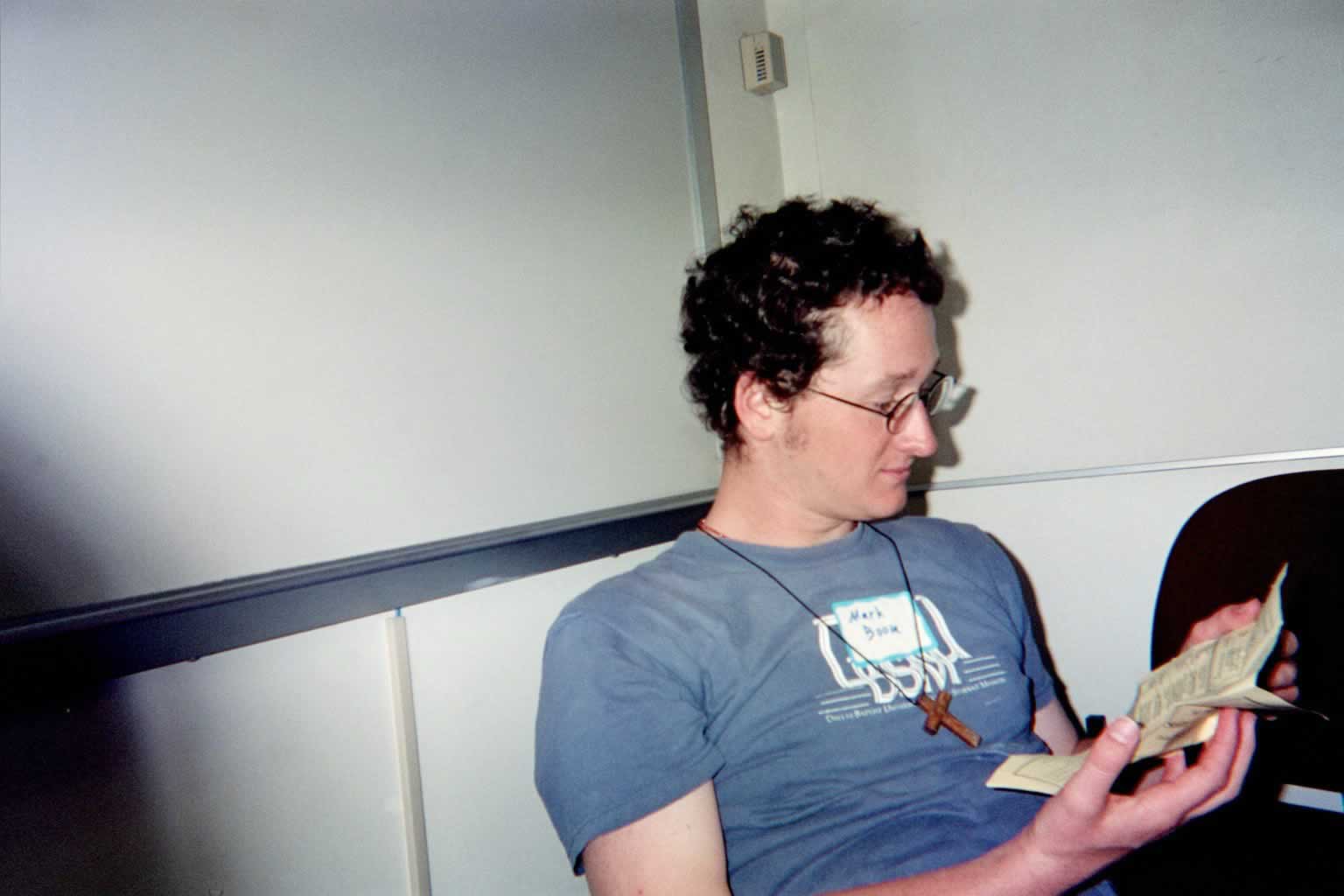 picture of a man in glasses sitting down reading a yellow paper