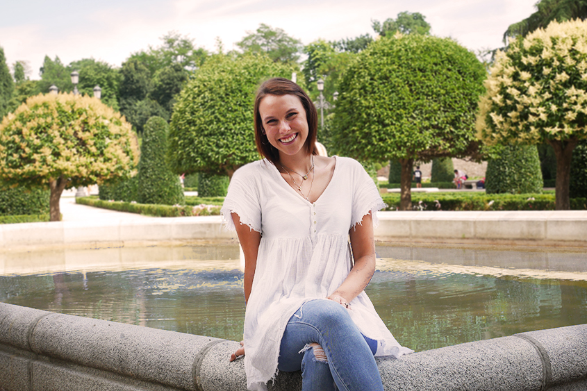 Corinna sits on a fountain in a Spanish garden