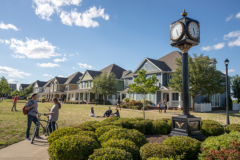 Students talk, have a picnic, play football, and walk to class on the yard in between the townhomes on campus.