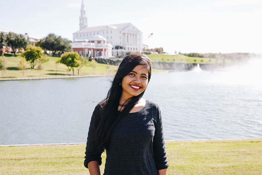 Ranjita poses in front of swan lake with the chapel and nation hall in the background.