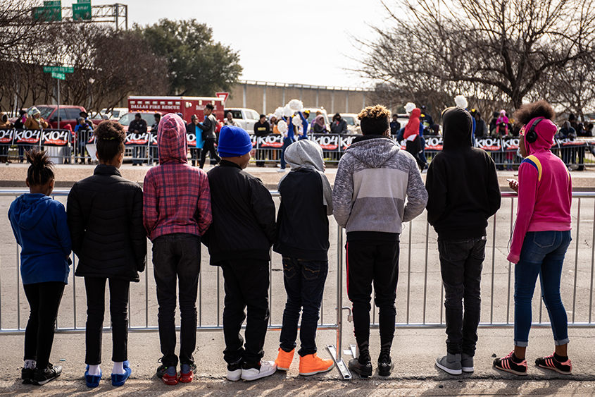 8 young children are standing in a row, waiting for a parade to begin. 