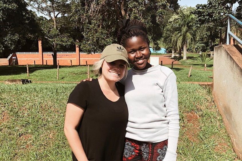 A female DBU Student is standing next to a girl from Uganda in Uganda. 