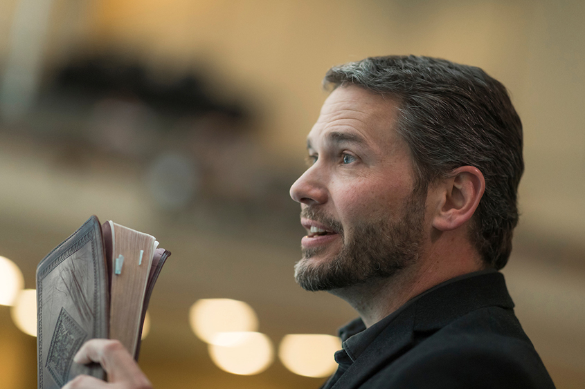 A man is standing holding a bible.