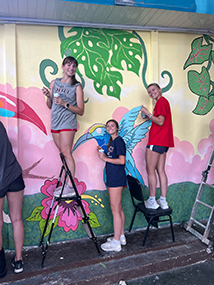 three girl DBU athlete volunteers from the volleyball and soccer teams painting mural