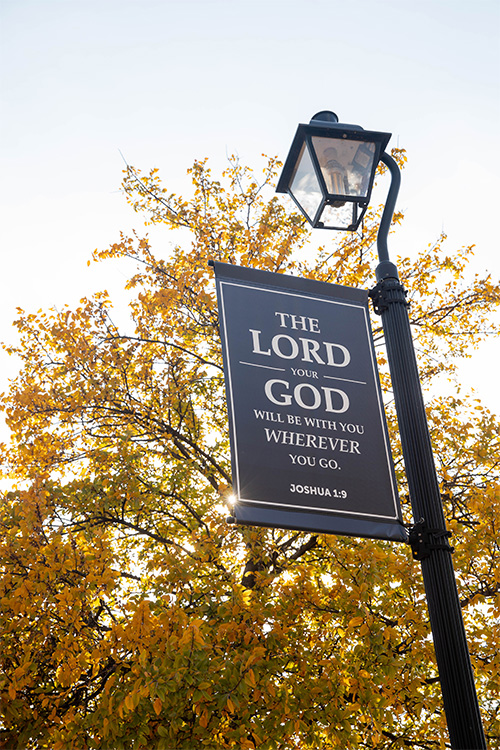 dbu lamppost with verse banner in front of an autumn tree