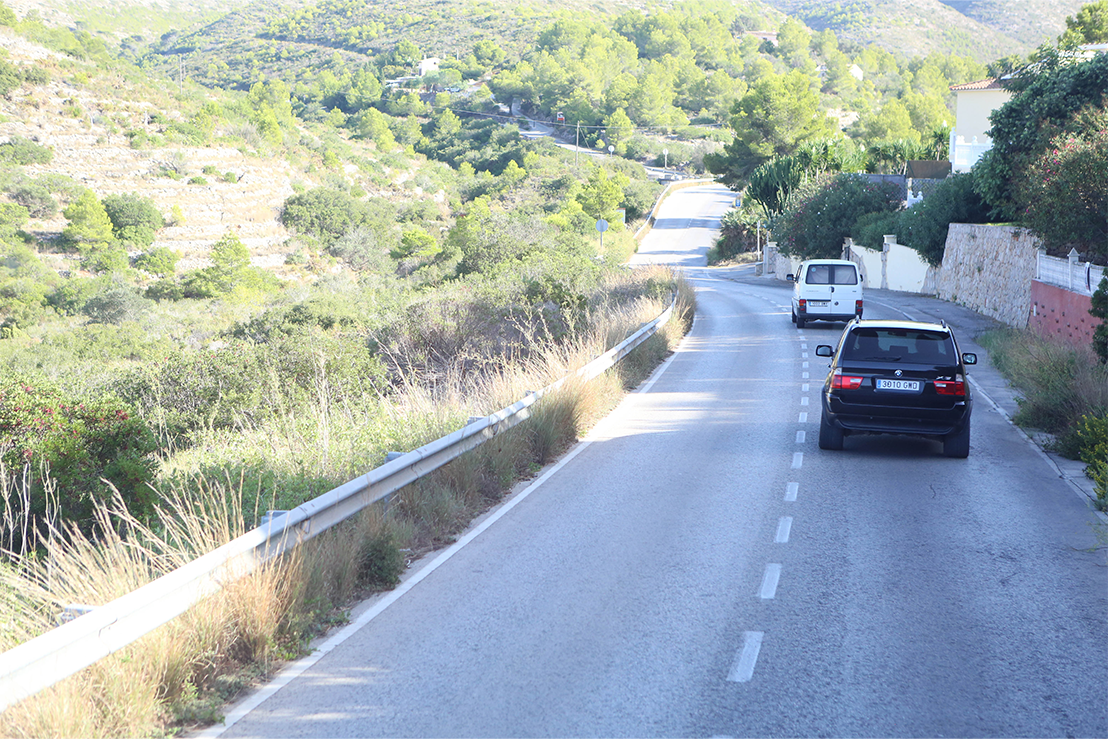 Winding road with two cars surrounded by green hills and trees on a sunny day