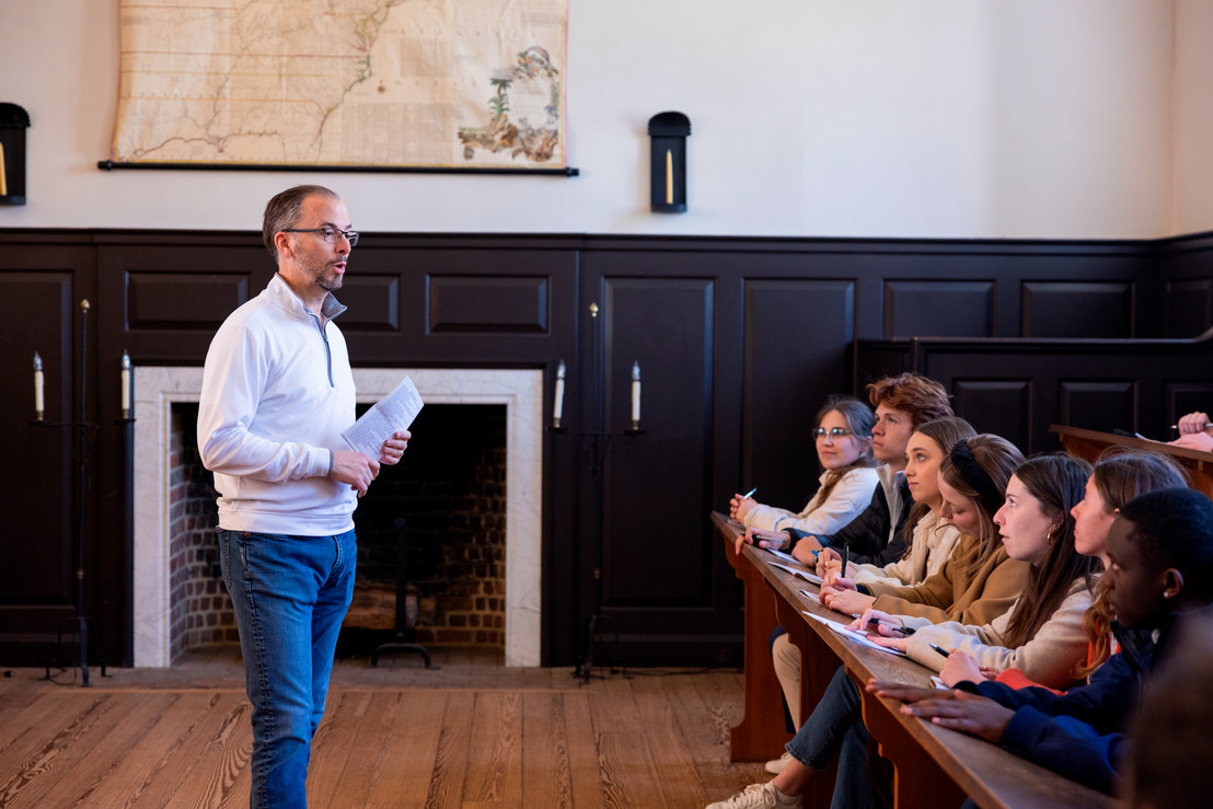 man lecturing attentive Dallas college students taking notes while seated at wooden desks