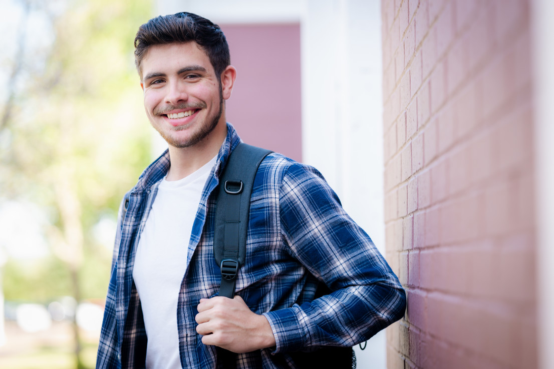 college student standing outside in Dallas, Texas with a backpack by a brick building