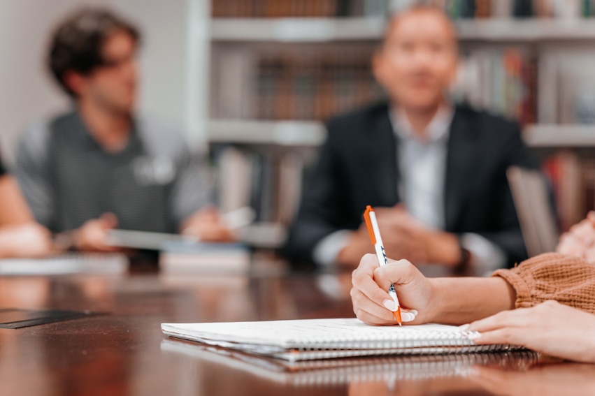 A girl holds a pen sitting at a table in a business meeting