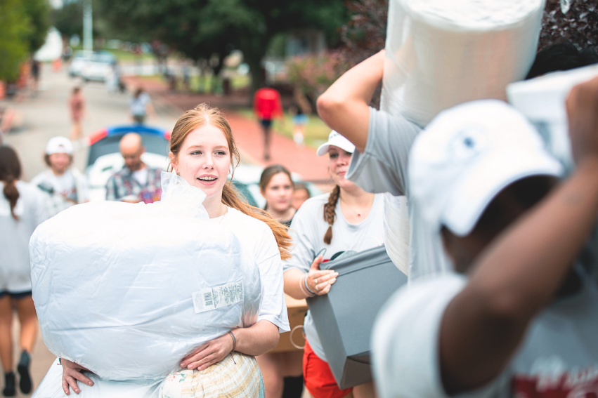 A girl carries her luggage into the dorm, surrounded by other students carrying their luggage