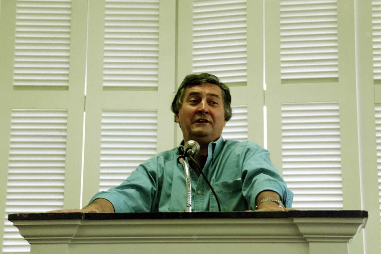 picture of Paul Marshall standing in front of a podium speaking wearing a green shirt
