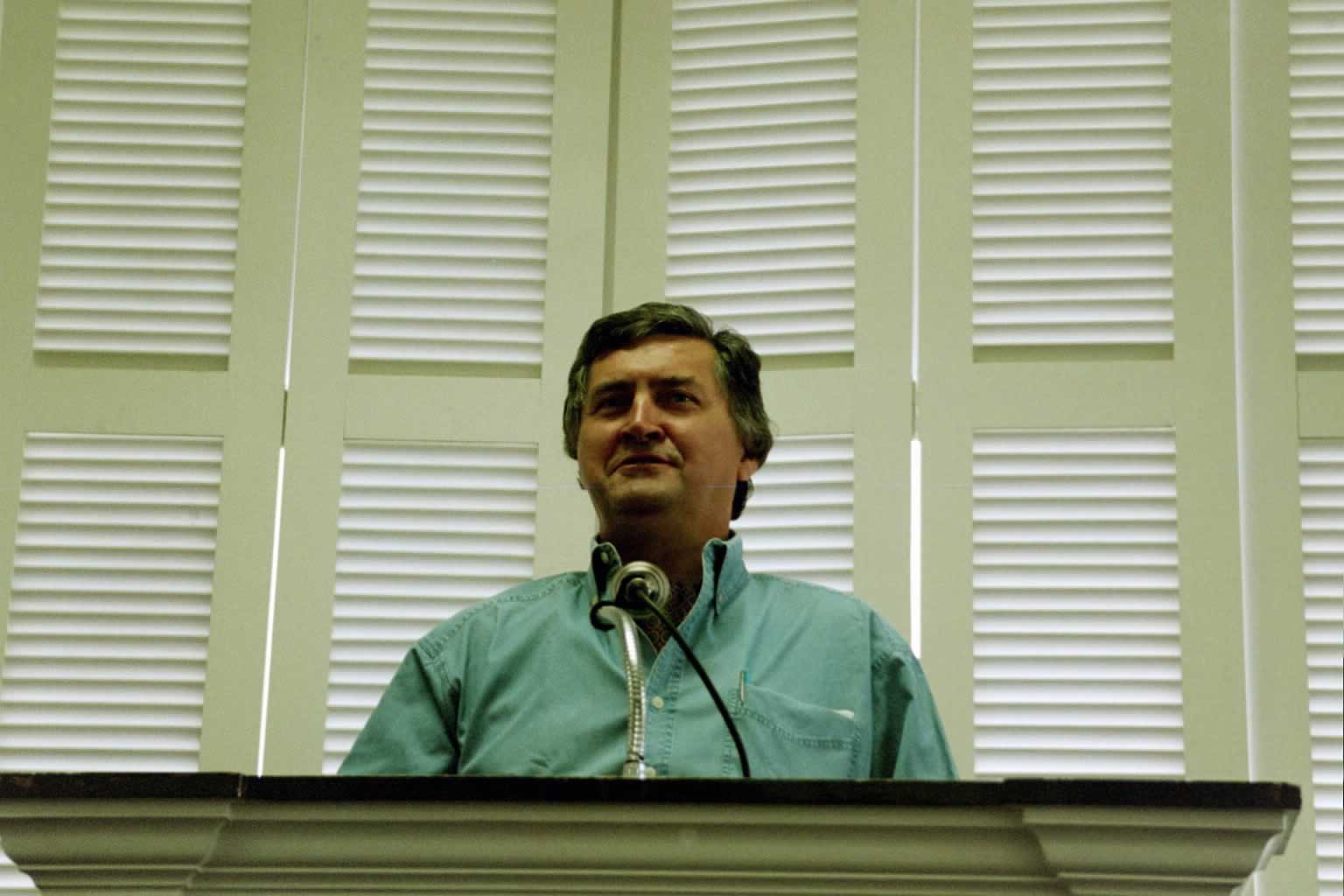 picture of Paul Marshall standing in front of a podium speaking wearing a green shirt