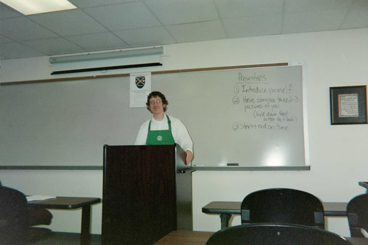 picture of a man with glasses standing behind the podium while wearing an apron