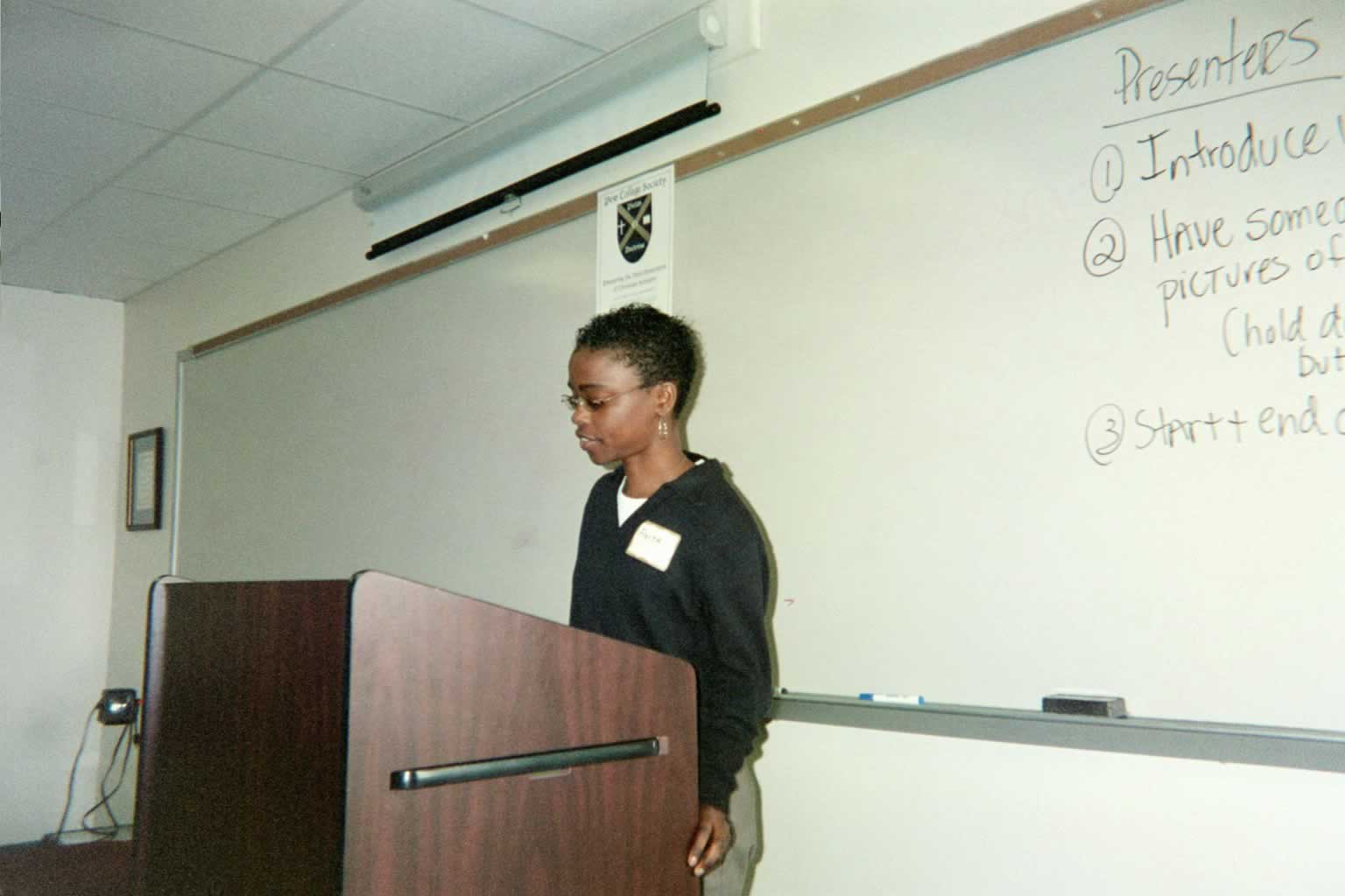 picture of a woman wearing glasses standing behind a podium speaking