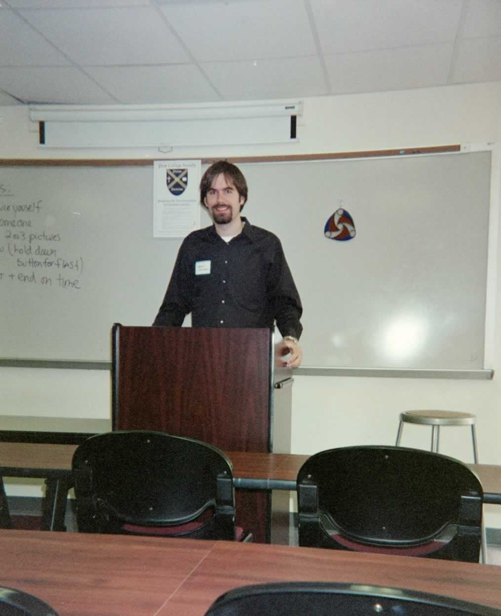 picture of a man standing in a classroom behind a podium smiling