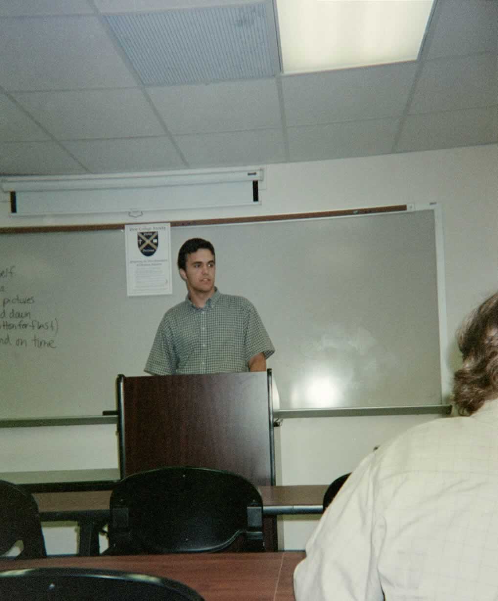 picture of a man in a checkered shirt standing behind a podium speaking