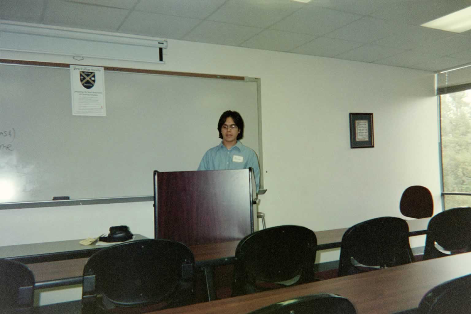 picture of a man in glasses standing behind a podium speaking