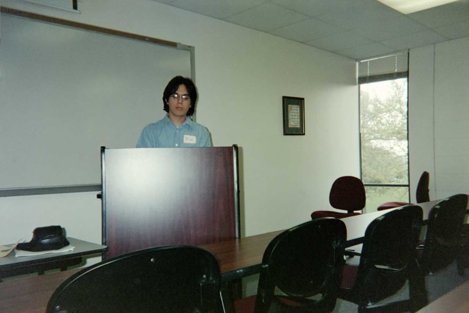 picture of a man in glasses standing behind a podium speaking