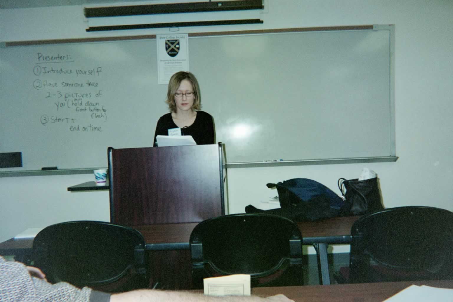 picture of a woman standing behind a podium reading from a piece of paper