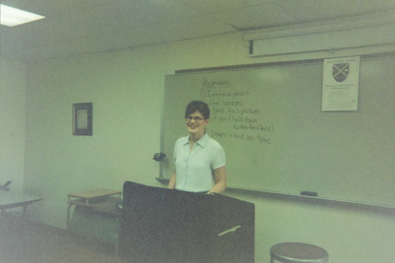 picture of a woman smiling behind a podium in a classroom