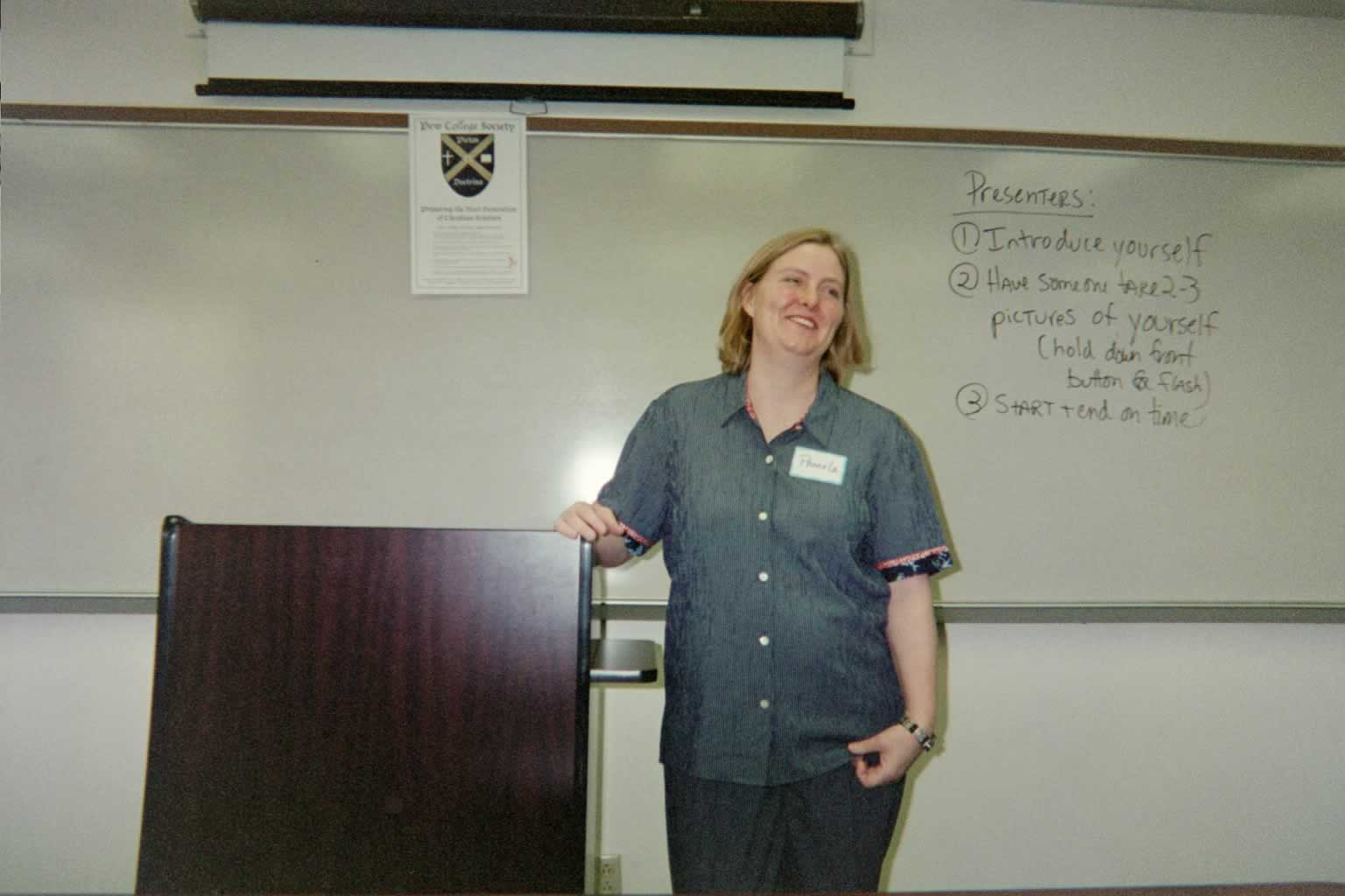 picture of a woman smiling next to a podium in a classroom