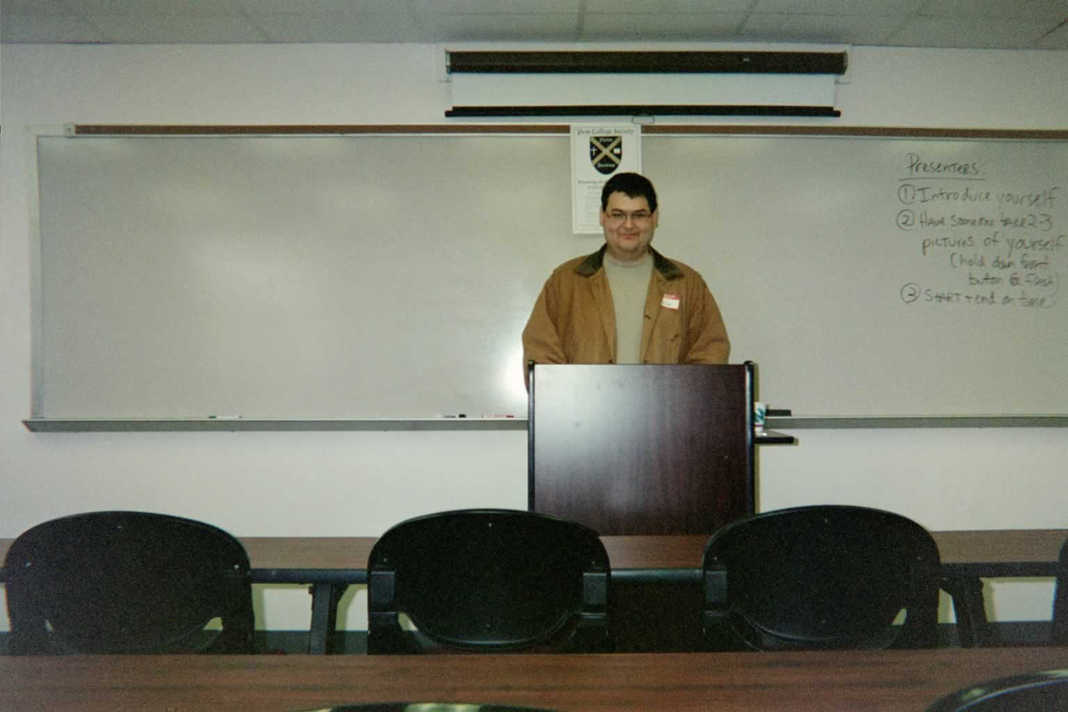 picture of a man in glasses standing behind the podium in a classroom smiling