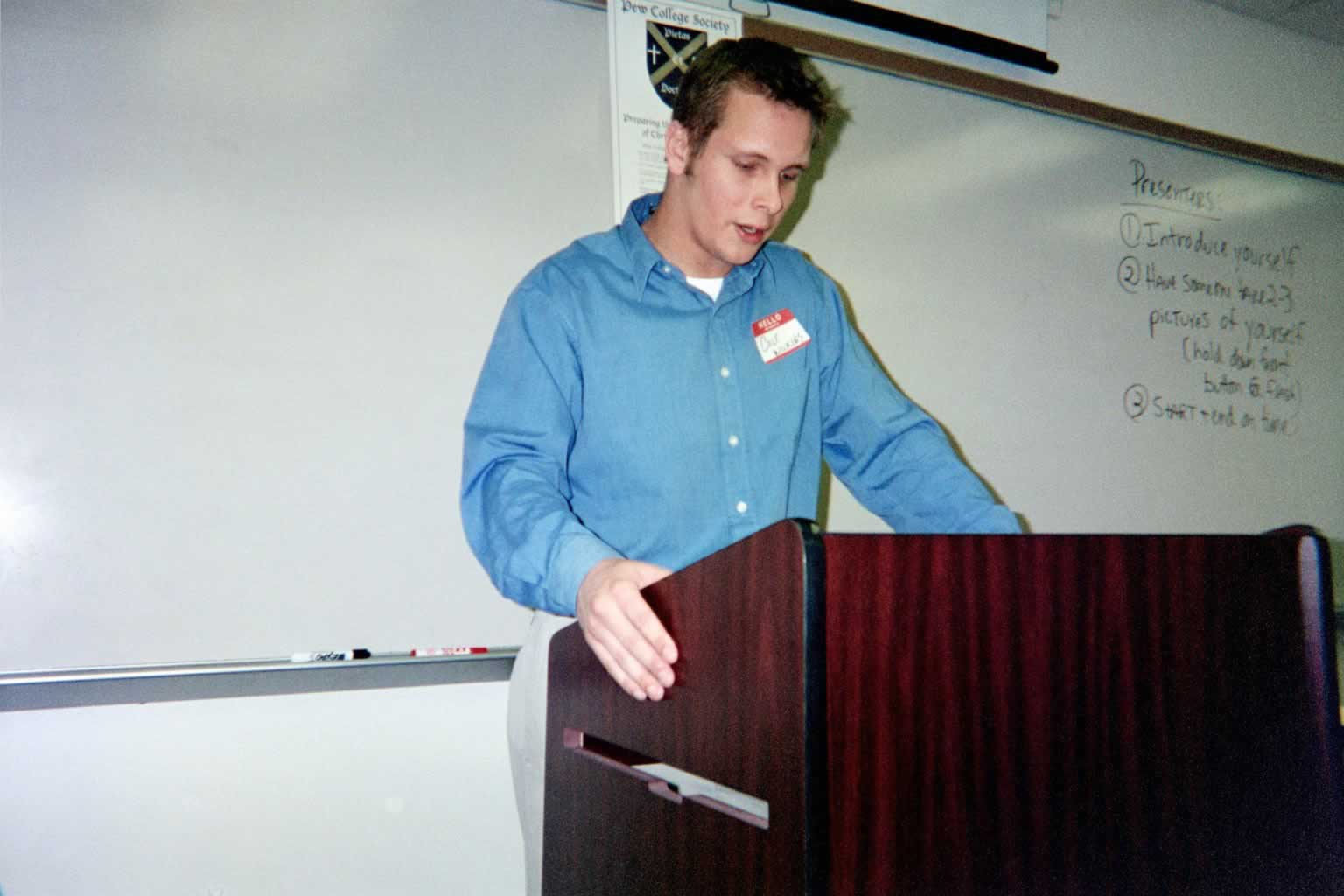 picture of a man in a blue shirt standing behind a podium in a classroom