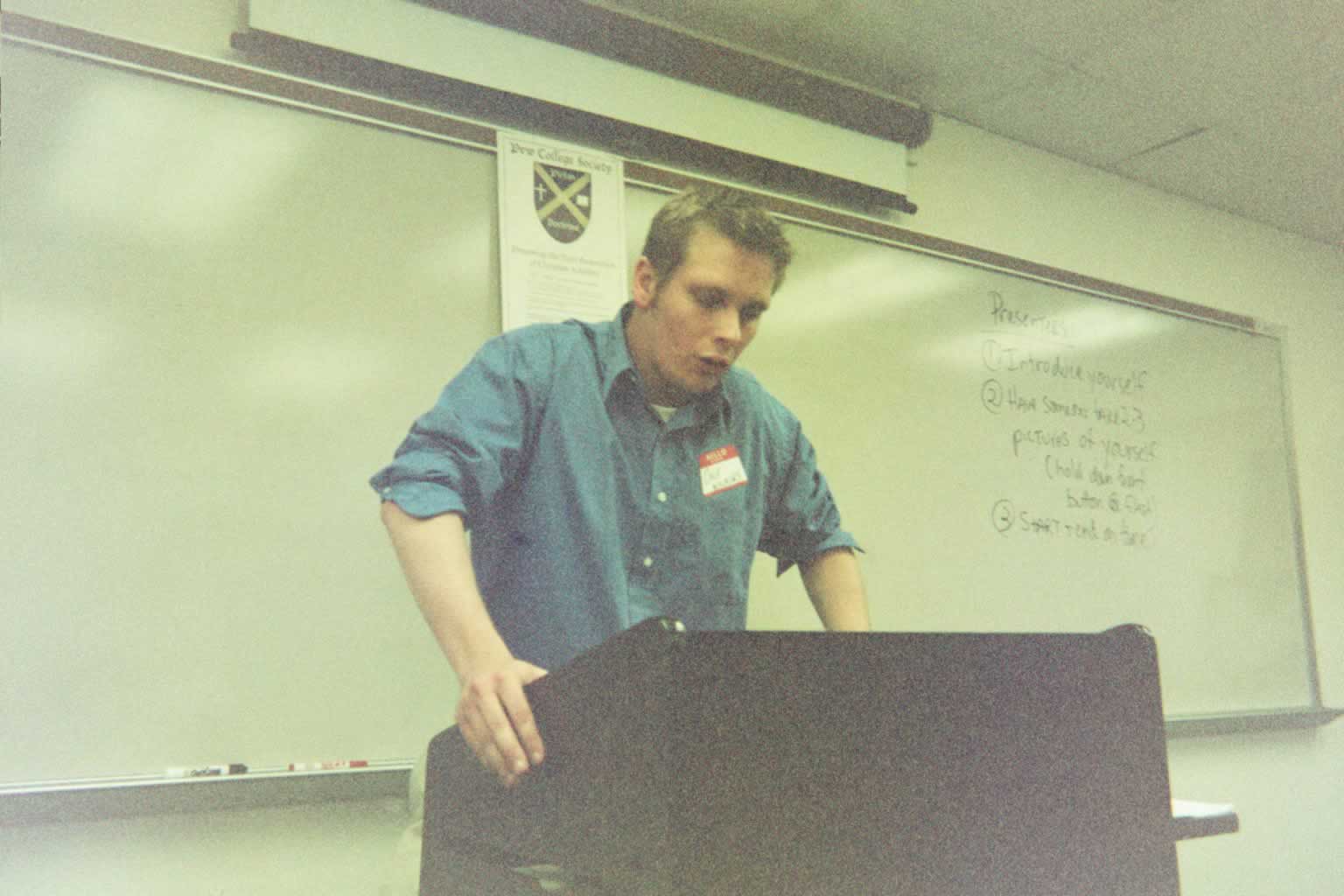 picture of a man in a blue shirt standing behind a podium speaking
