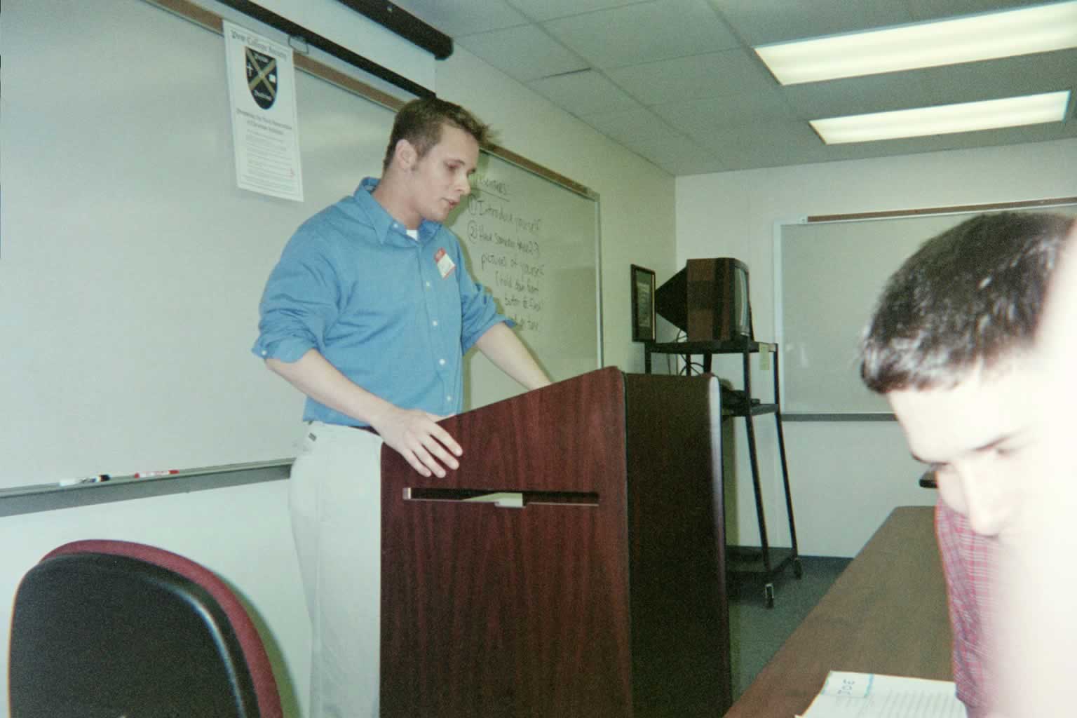 picture of a man in a blue shirt standing behind a podium speaking