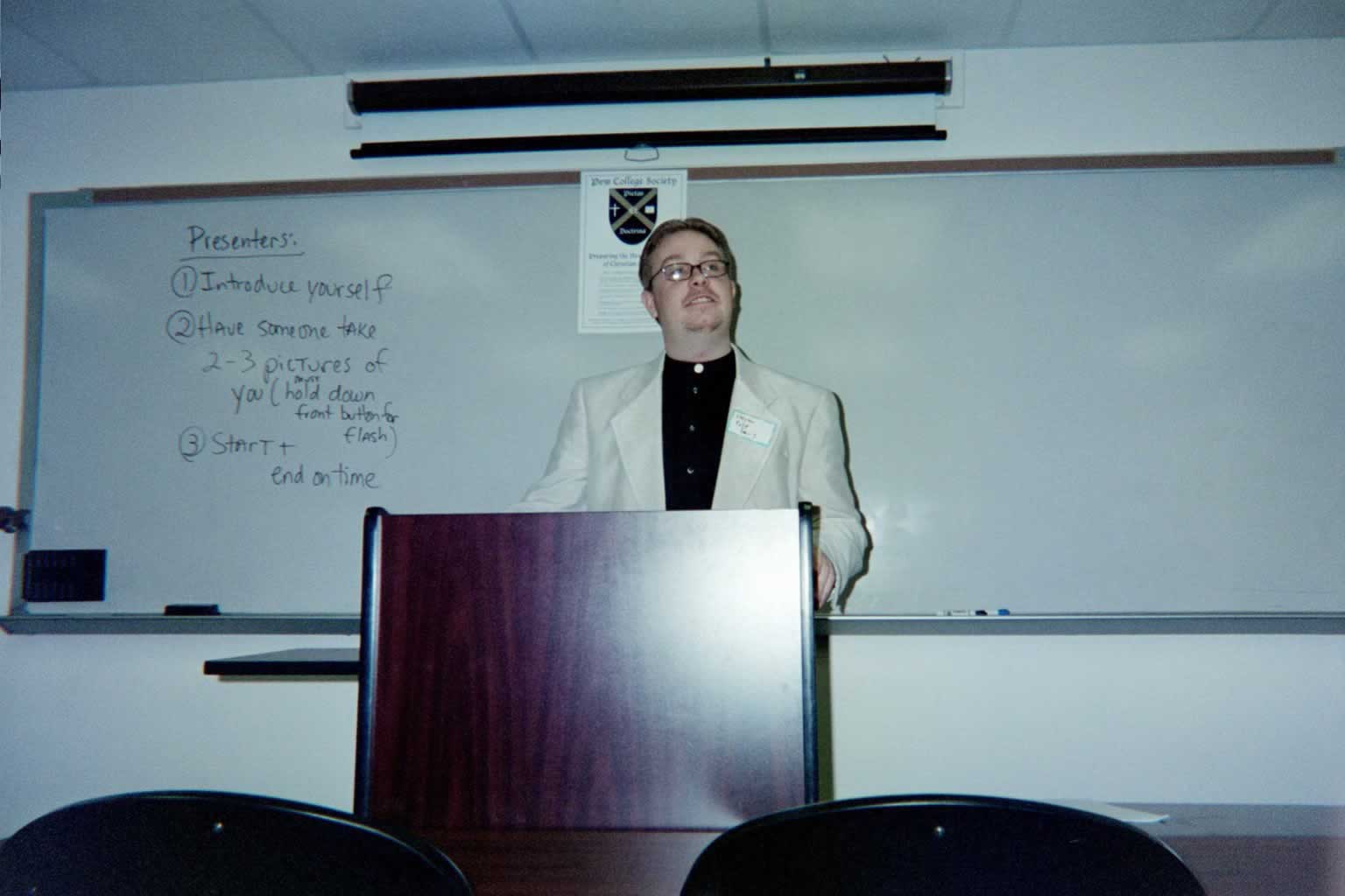 picture of a man wearing glasses standing behind a podium talking