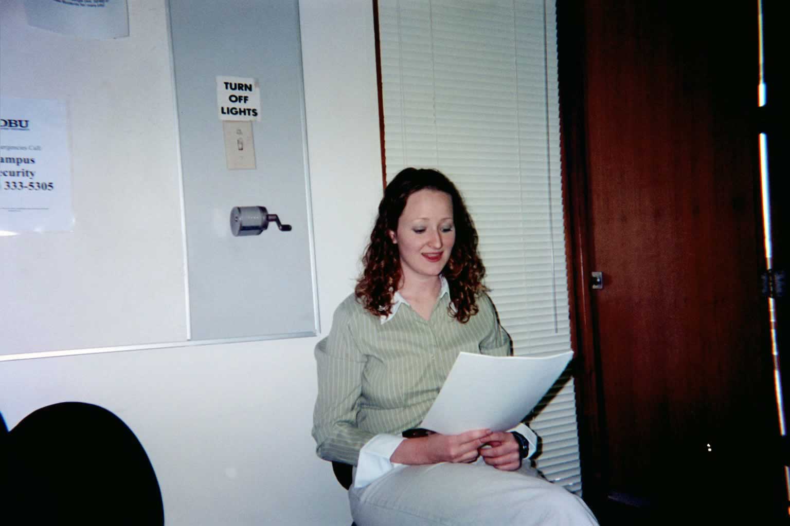 picture of a woman in a green shirt sitting by a door reading off of a paper