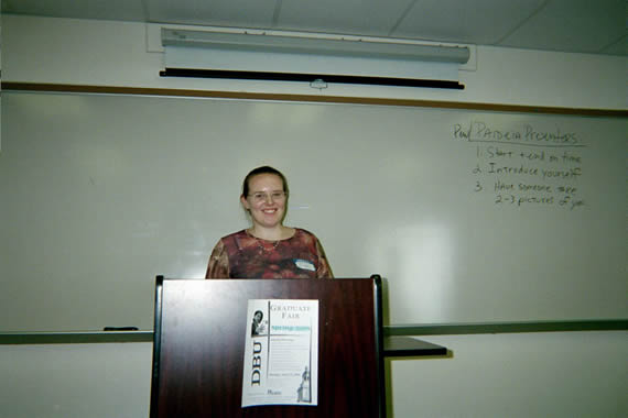 picture of a woman in glasses standing behind a podium smiling