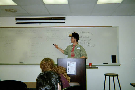 picture of a man standing behind a podium while speaking and pointing to the whiteboard