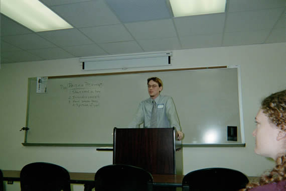 picture of a man with glasses standing in front of a podium speaking