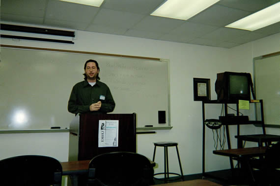 picture of a man standing at the front of a clasroom behind a podium
