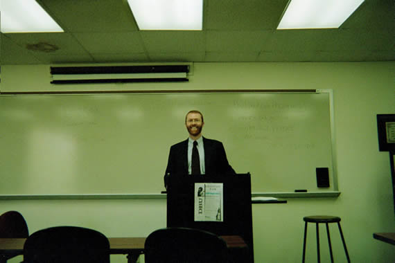 picture of a man in a suit standing behind a podium in a classroom
