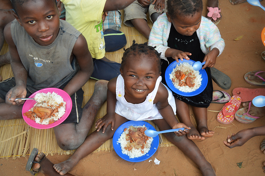 A sweet baby girl eats with her friends in Mozambique