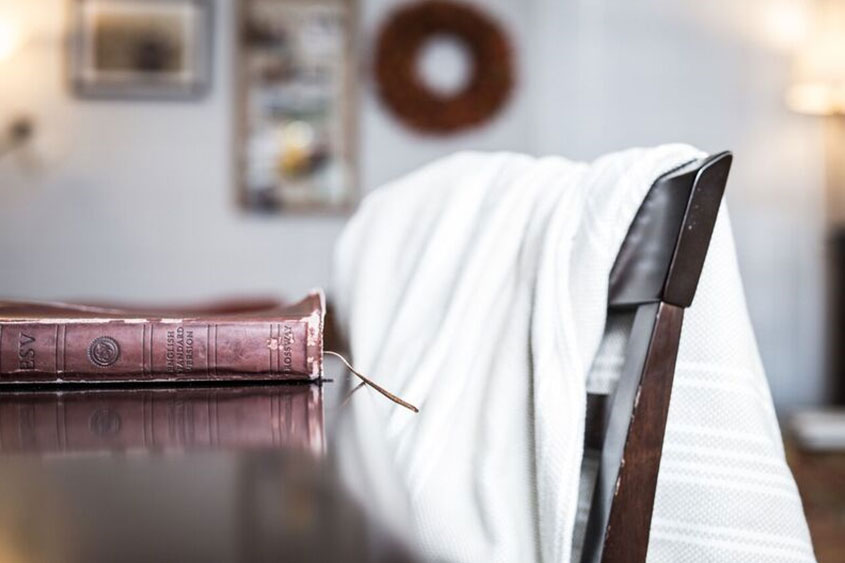 A bible rests on the dining table with the sunrise peeking through the window