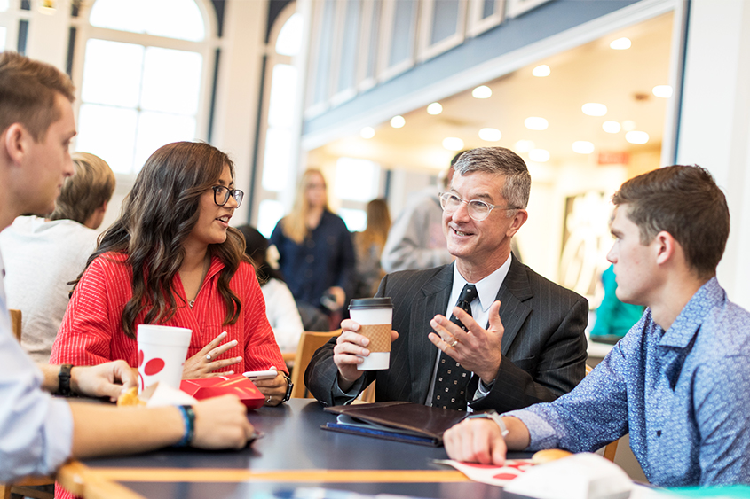 Dr. Ross O'Brien fellowships with students at a table at Chick-fil-a on campus