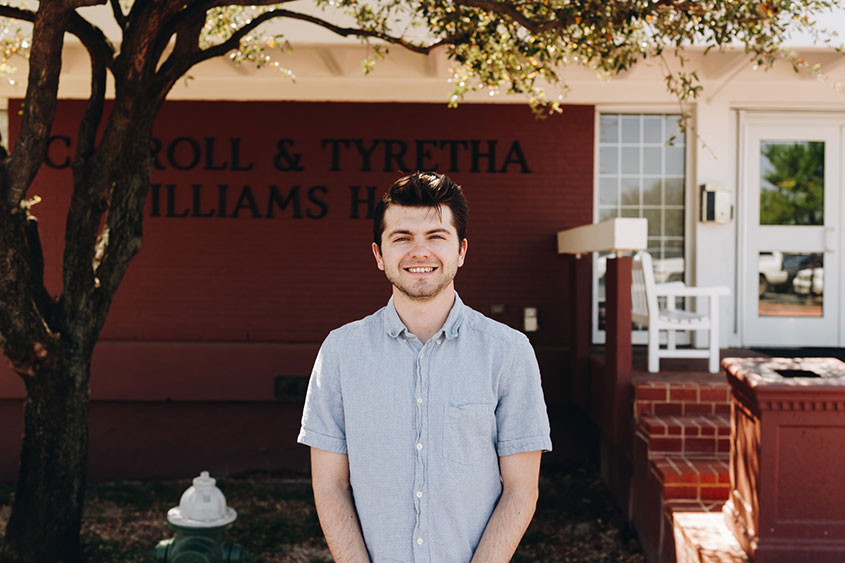 A male student is standing in front of Williams dorm. 