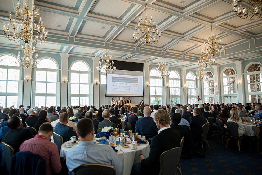 Guests at the Lion's U event are sitting at tables listening to a presentation. 