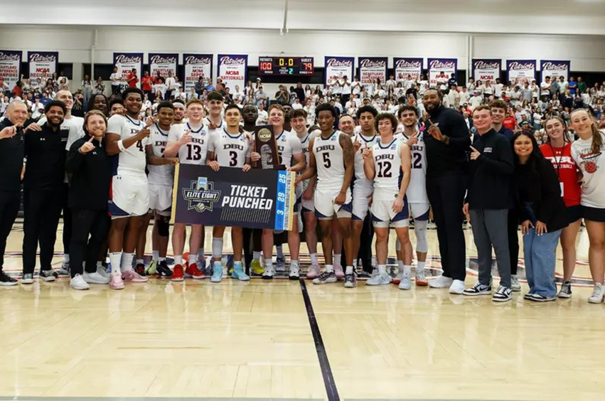 DBU Patriots men's basketball team standing on the basketball court with crowd in background