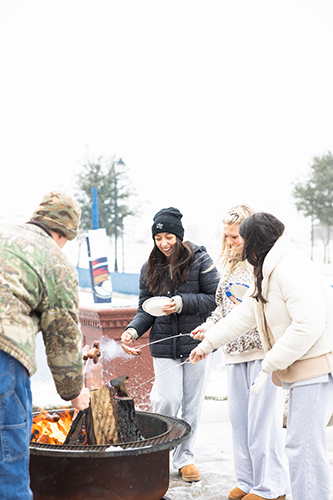 college students roasting hotdogs over a fire during the Dallas winter snow for January 2026