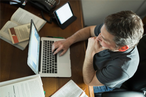 male student working on computer while being surrounded in open books